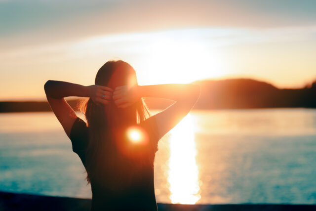 Frau, die am See steht und den Sonnenuntergang beobachtet
