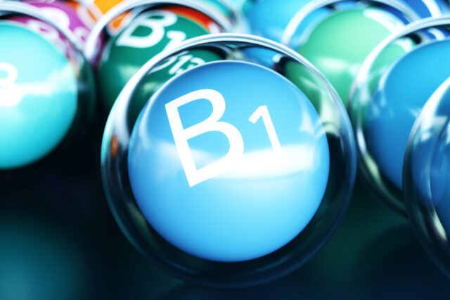 Vitamin B1 Schriftzug auf blauem Ball umrandet von einem durchsigtigen Ball auf schwarzem Boden