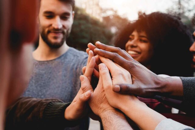 Eine Gruppe von Menschen legt ihre Hände als Zeichen des Teamgeists und der Zusammenarbeit aufeinander.