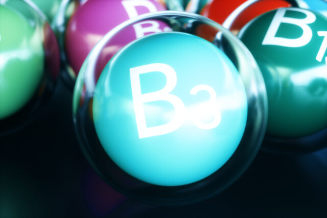 Vitamin B3 Schriftzug auf türkisfarbenem Ball umrandet von einem durchsigtigen Ball auf schwarzem Boden.