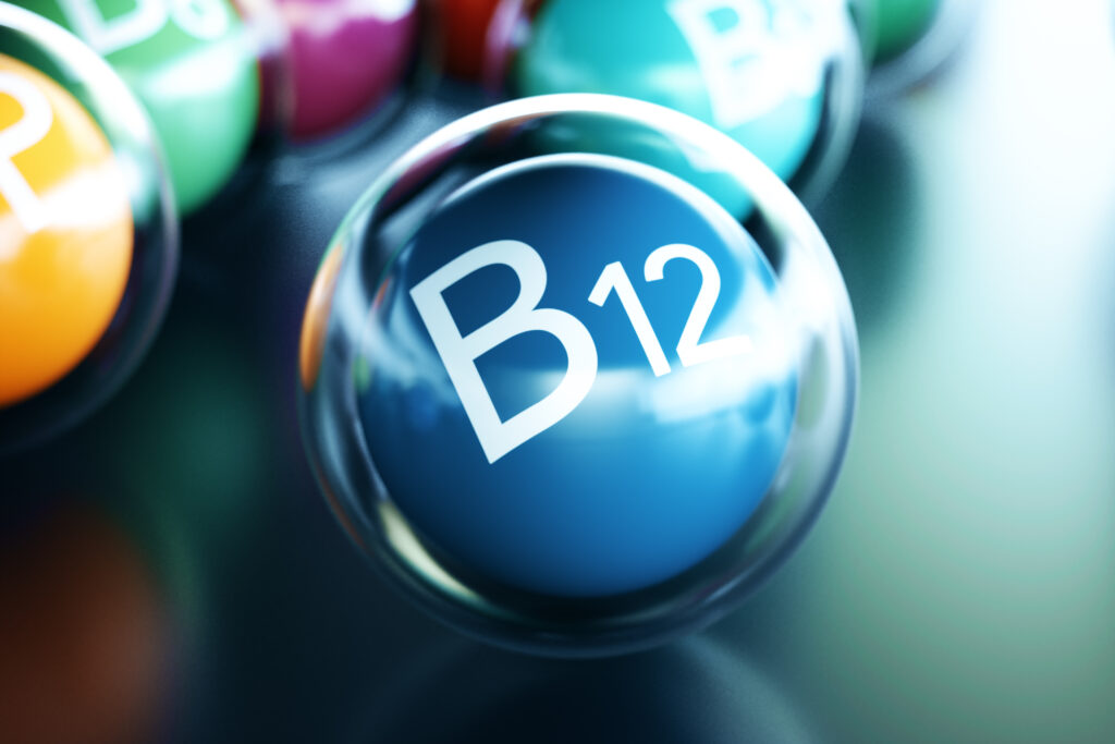 Vitamin B12 Schriftzug auf dunkelblauem Ball umrandet von einem durchsigtigen Ball auf schwarzem Boden.