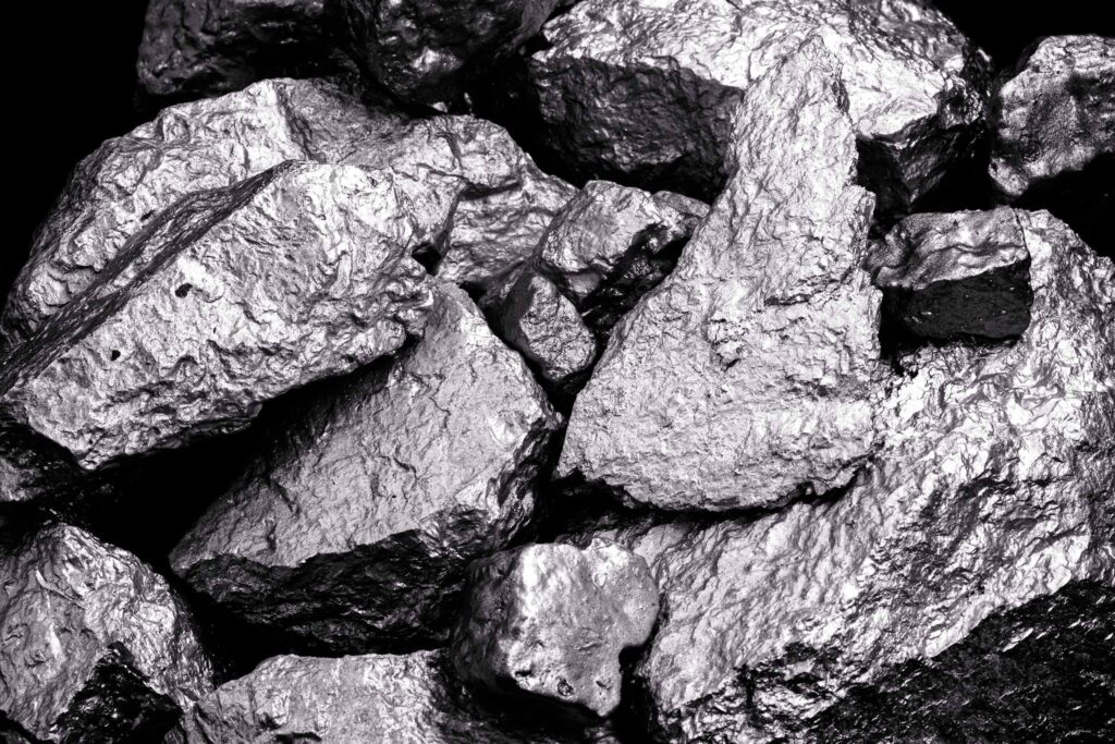 Detailansicht von rauen, metallisch glänzenden Gesteinsbrocken oder Erzstücken in dunklen Grautönen vor schwarzem Hintergrund.