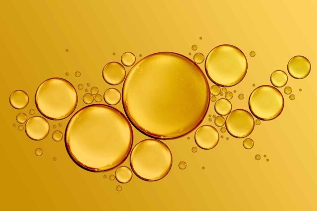 Eine künstlerische Makroaufnahme von verschieden großen, goldenen Omega-9-Öltropfen, die auf einer hellgelben Oberfläche schweben und Reinheit sowie Konzentration verdeutlichen.