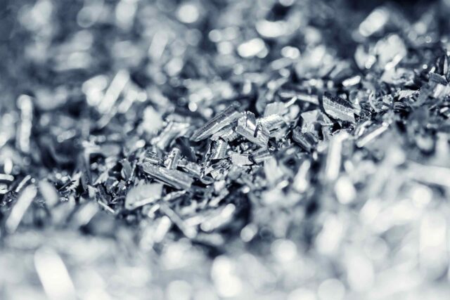 Detailansicht von dunklem, rauem Eisenerz mit metallischen Einschlüssen vor einem schlichten Hintergrund.