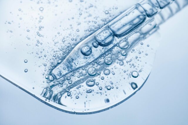 Pipette mit klarem, blaugrauem flüssigen Serum auf Glasuntergrund