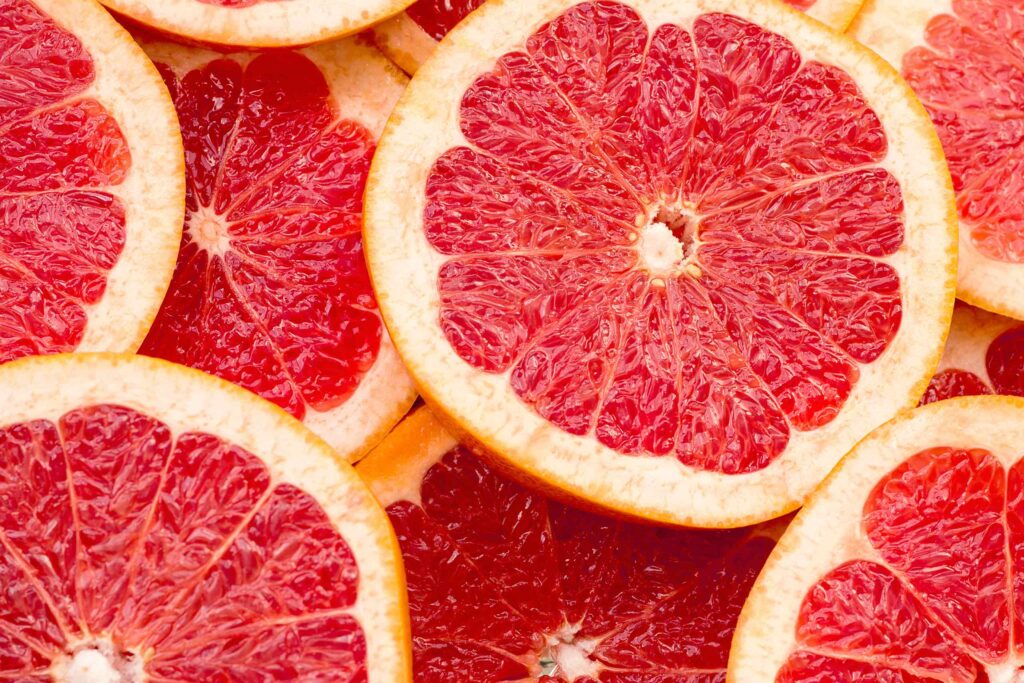 Mehrere aufgeschnittene Grapefruit-Scheiben mit saftigem, tiefrosa Fruchtfleisch in der Draufsicht.
