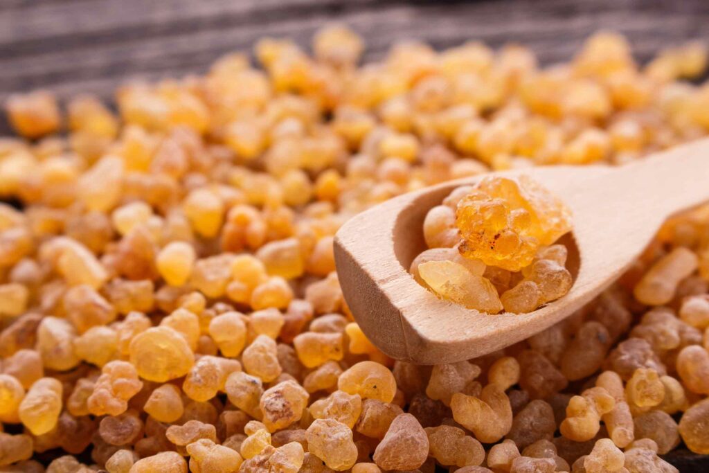 Eine große Menge goldgelber, harziger Weihrauch-Tränen auf einer Holzoberfläche, mit einigen Stücken auf einem kleinen Holzschaufel-Löffel.