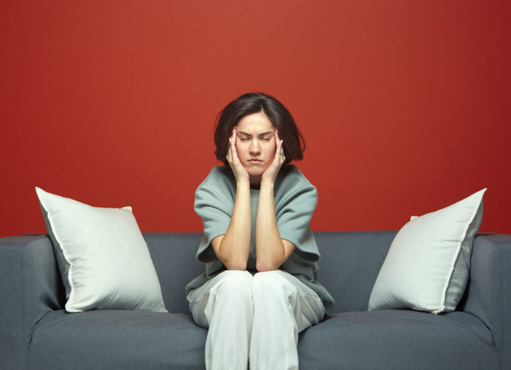 Young tired woman suffer headache closed eyes touching temples sitting on couch feeling exhausted by noisy neighbors. High quality photo